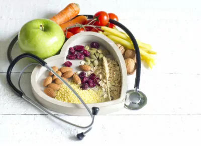 a bowl of nuts and whole grains surrounded by fruits and vegetables, with a stethoscope