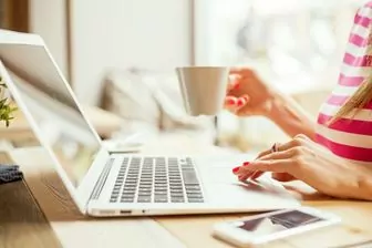 woman at her laptop holding a cup of coffee or tea